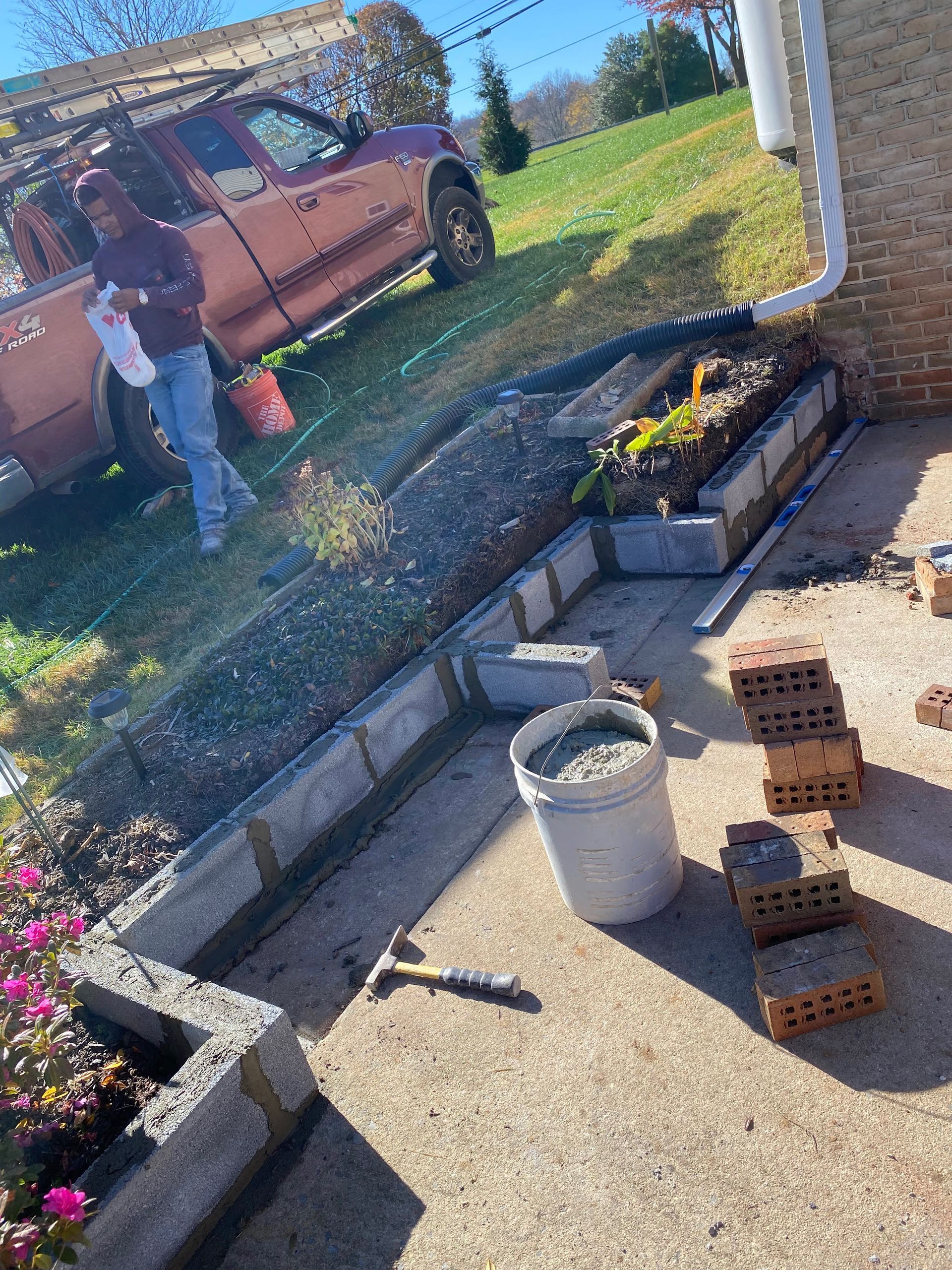 A bucket of cement is sitting on the ground where retaining wall is being built.