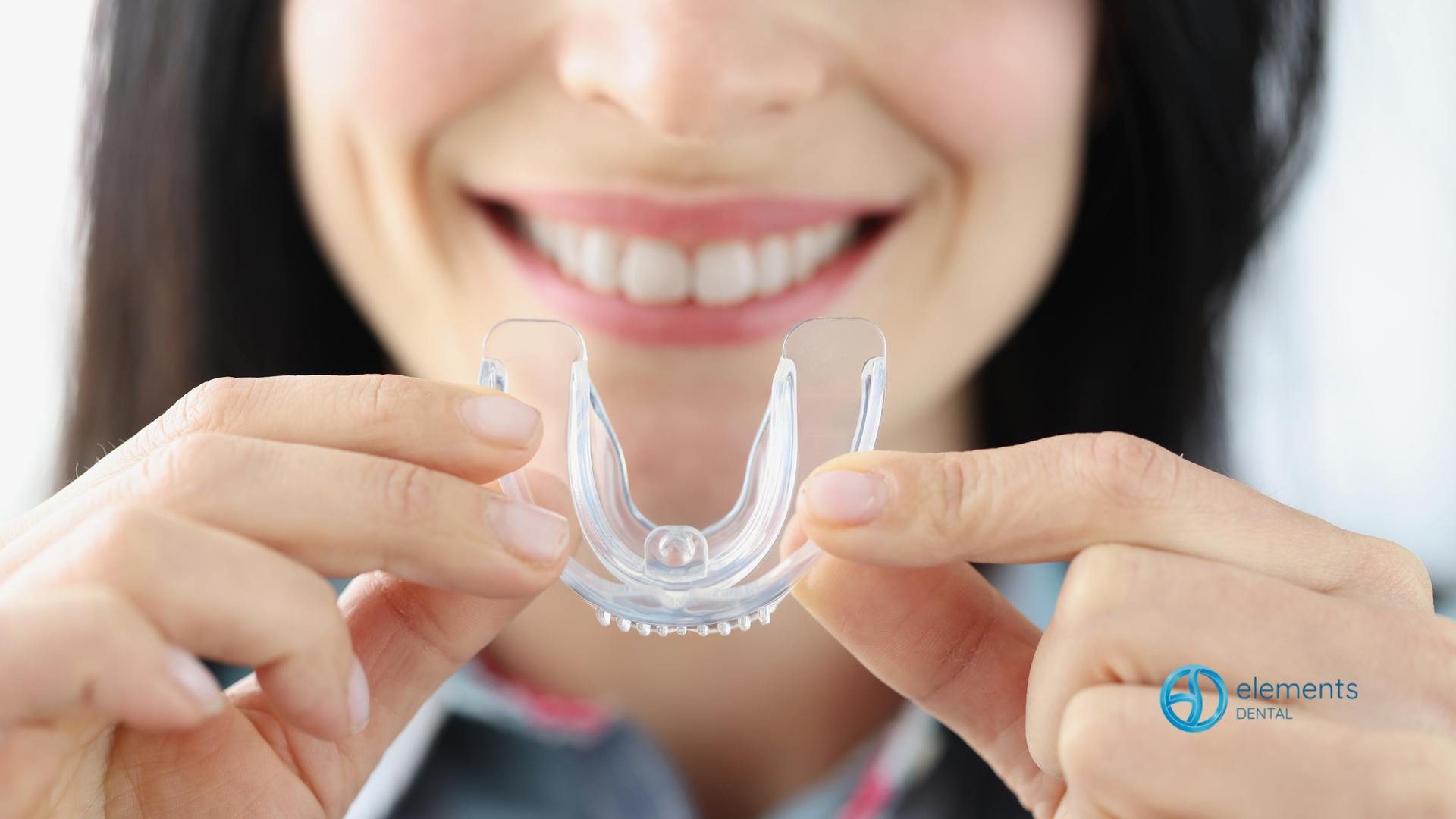 A woman is holding a clear mouth guard in front of her mouth.
