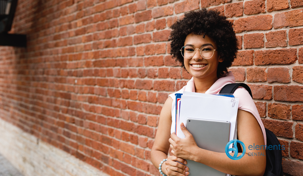 Smiling student with backpack and notebooks standing by a brick wall