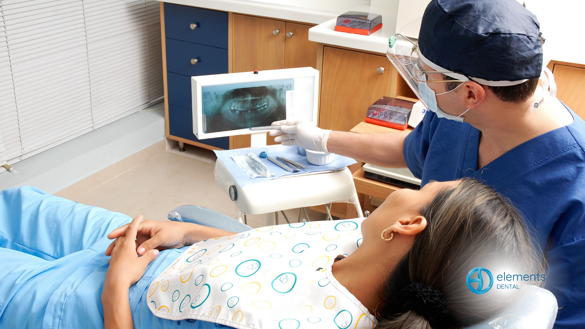 A woman is laying in a dental chair while a dentist examines her teeth.