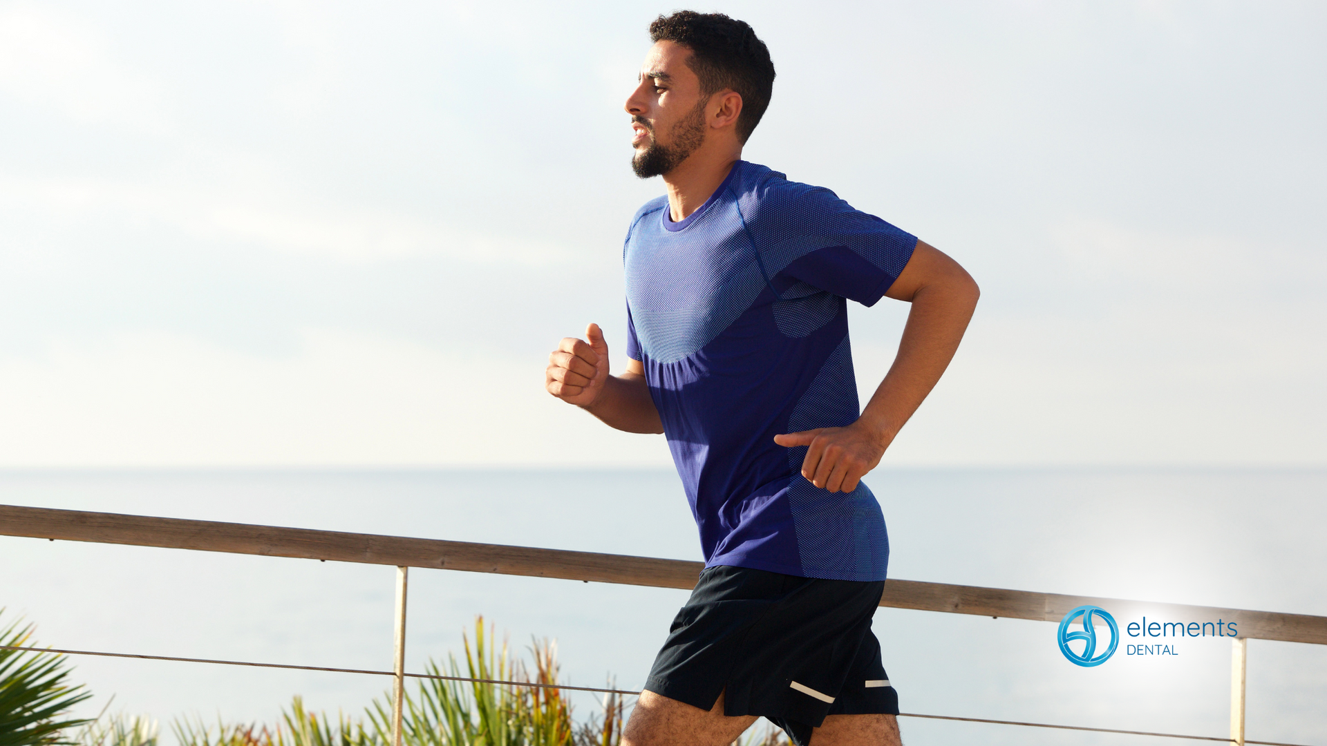 A man in a blue shirt and black shorts is running on the beach.