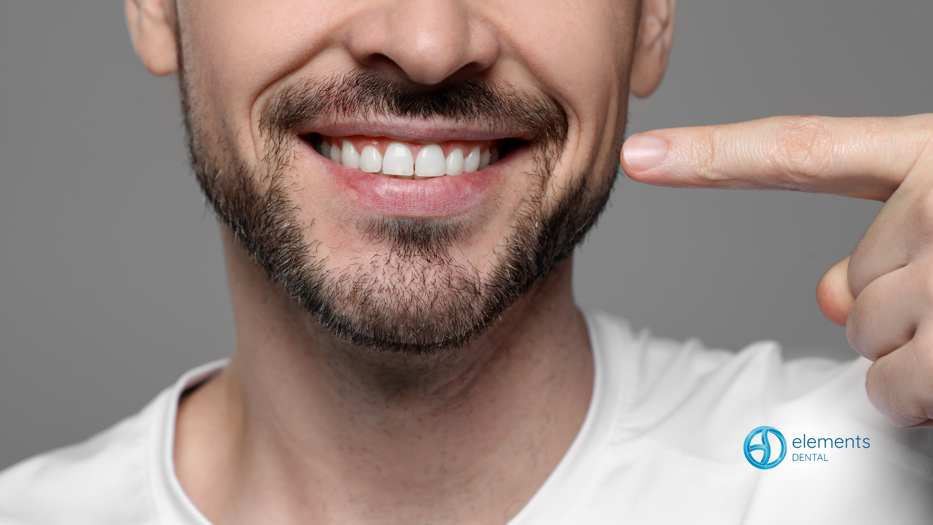 A man with a beard is pointing at his teeth.