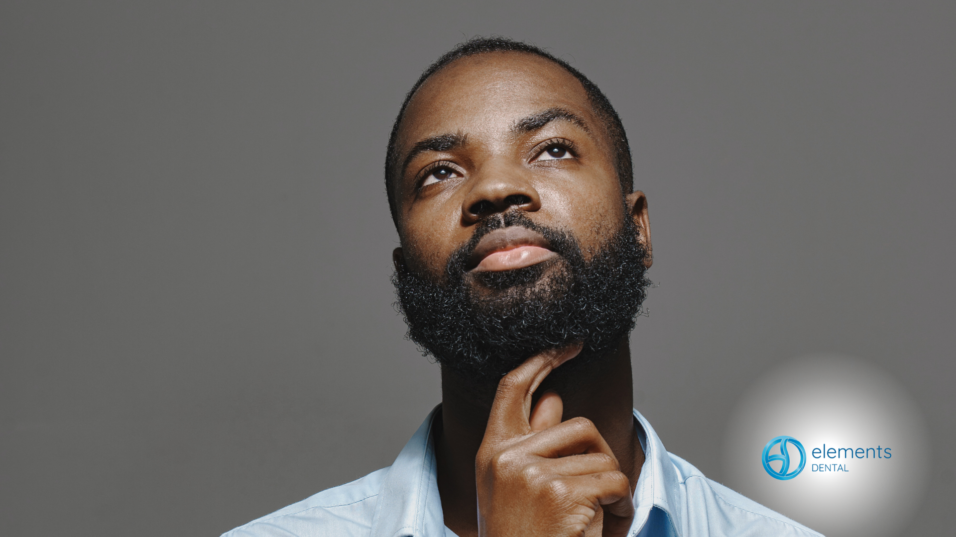 Person with thoughtful expression holding chin against a gray background, with a small logo in the corner