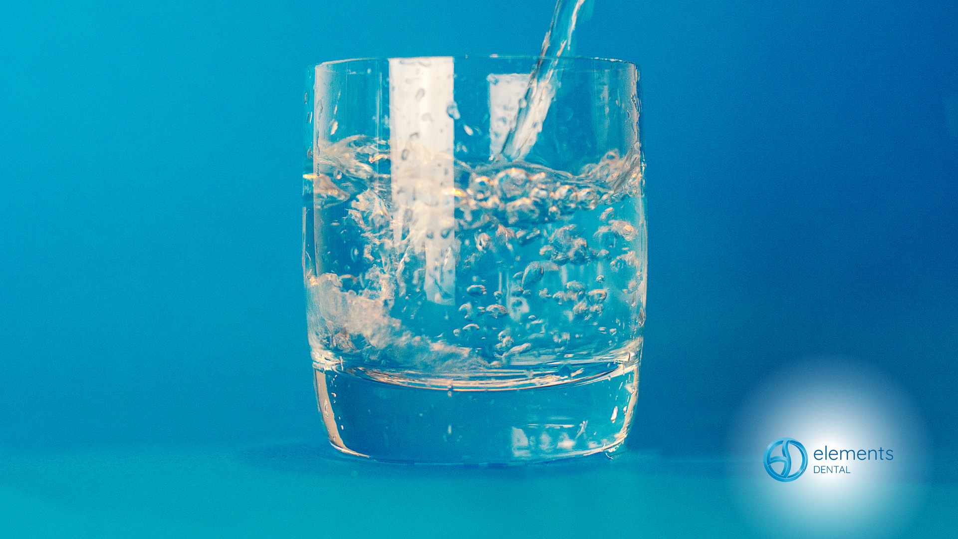 Water is being poured into a glass on a blue background.