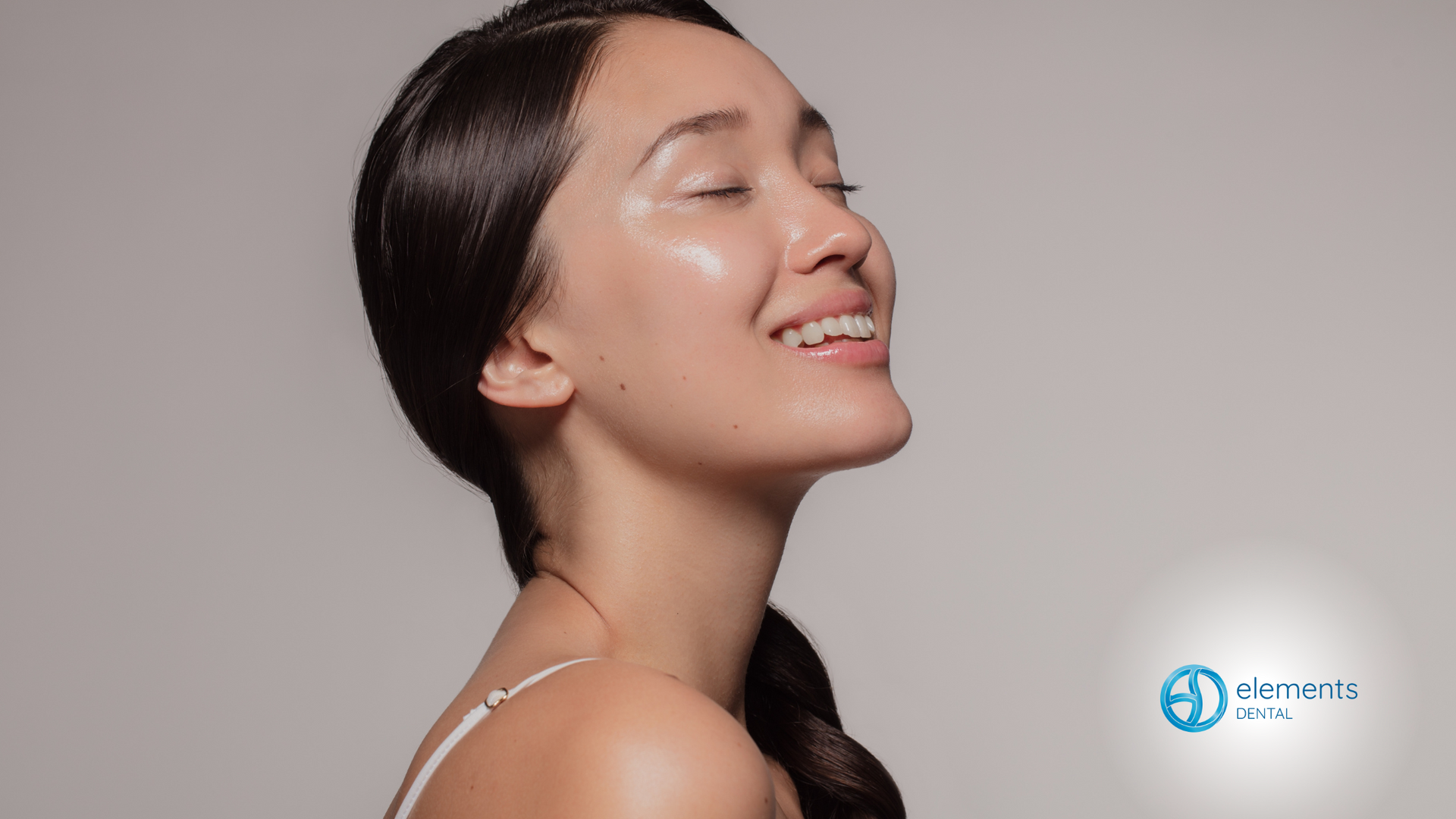A woman is smiling with her eyes closed and her hair in a ponytail.