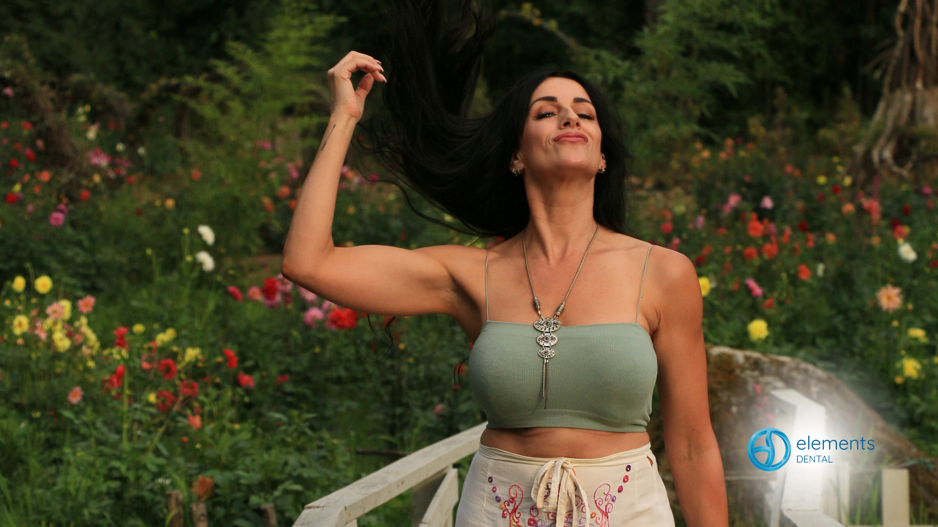 A woman is standing in a garden with her hair blowing in the wind.