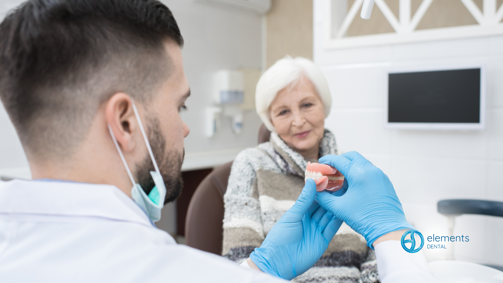 A dentist is holding a denture in front of an elderly woman.