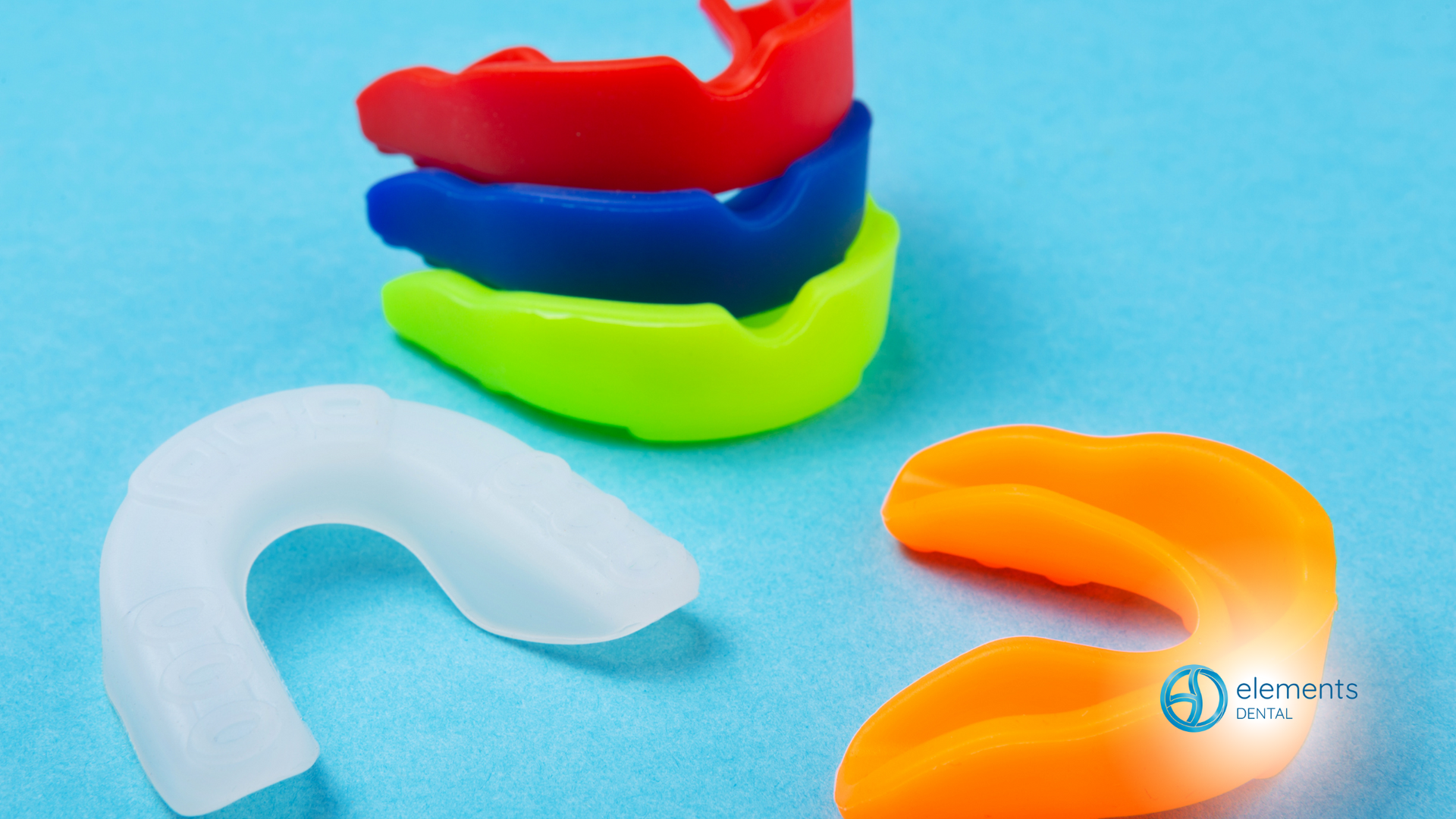A group of mouth guards of different colors are stacked on top of each other on a blue surface.