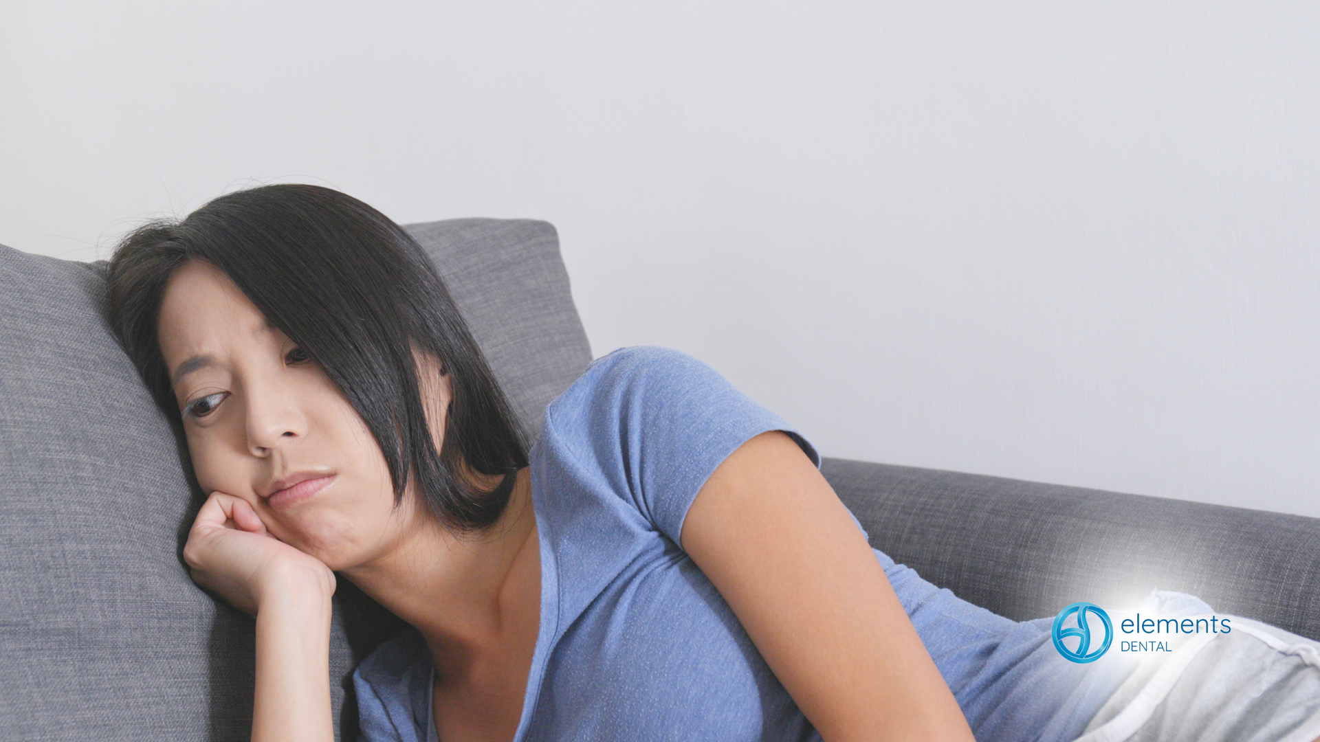 A woman is laying on a couch with her head on her hand.