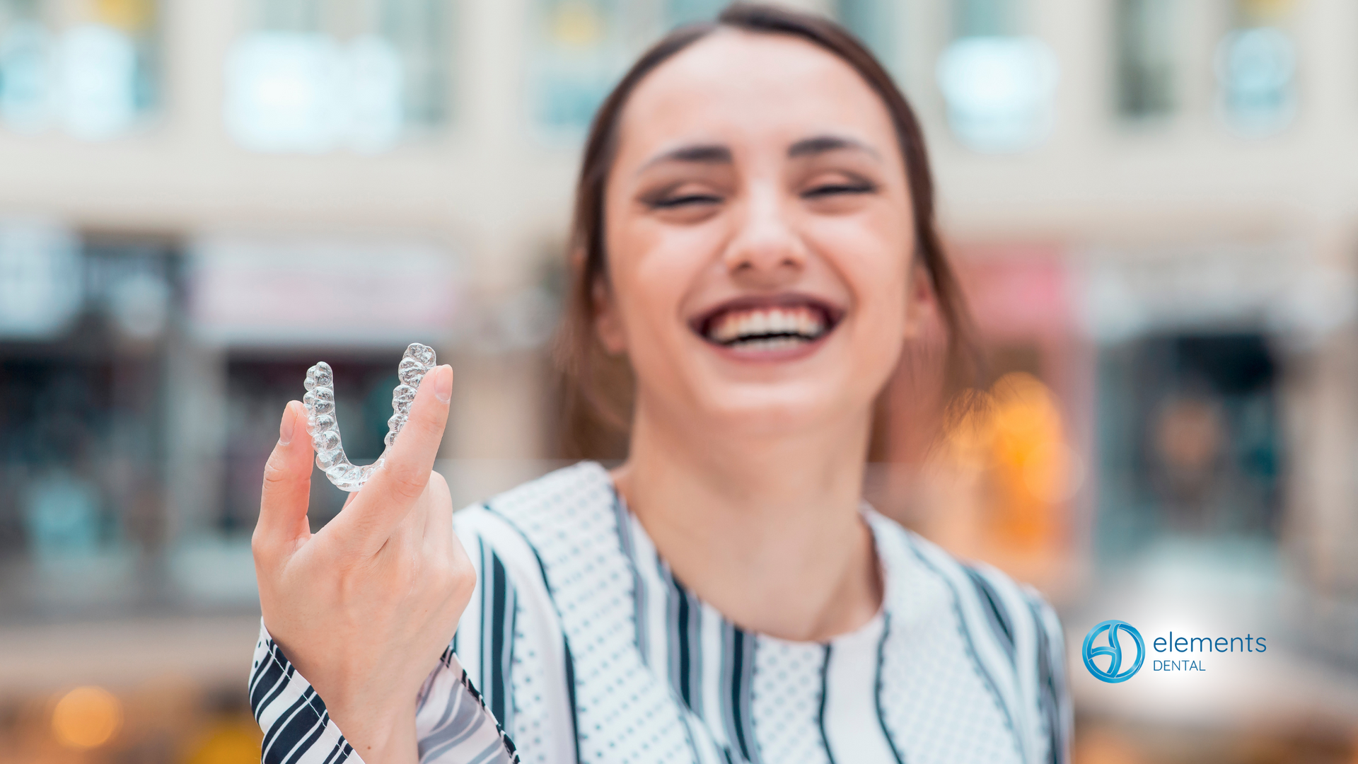 A woman is holding a clear retainer in her hand and smiling.