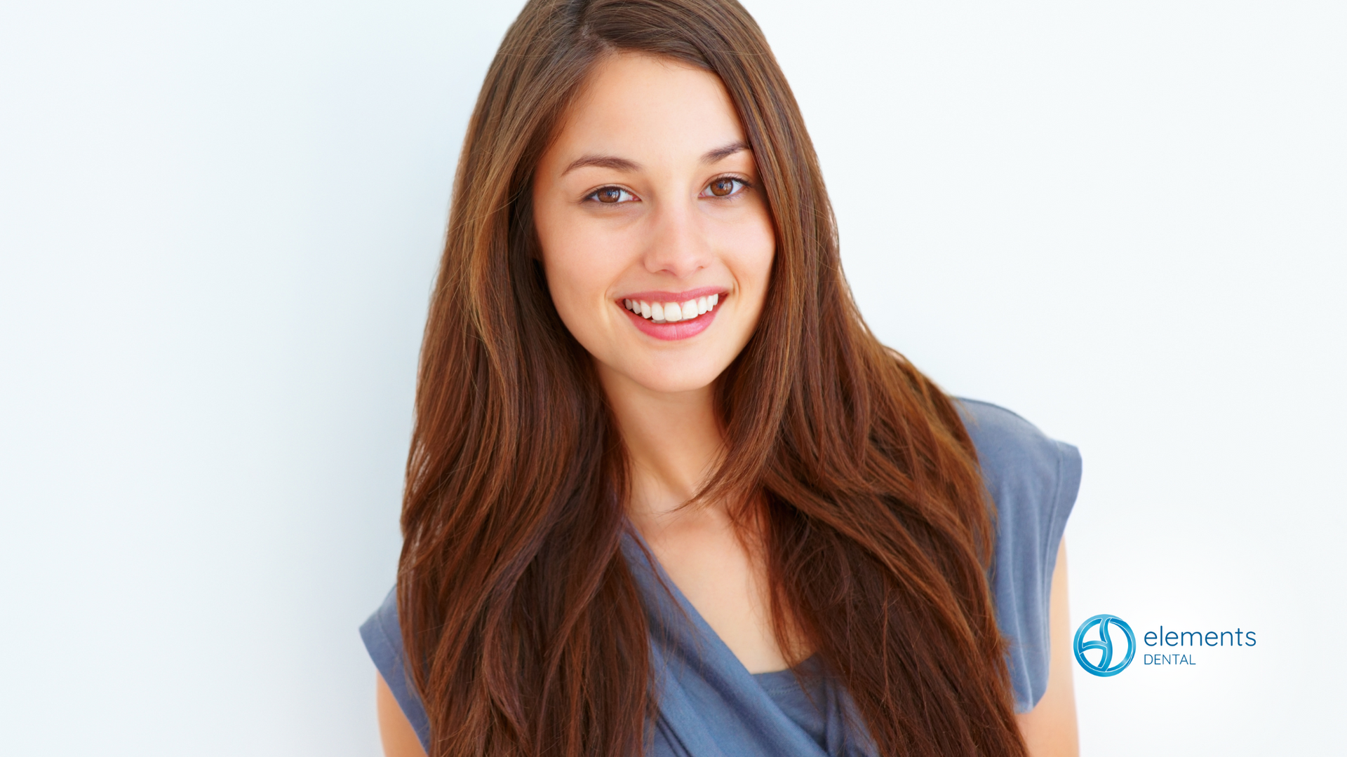 A woman with long brown hair is smiling and wearing a blue shirt.