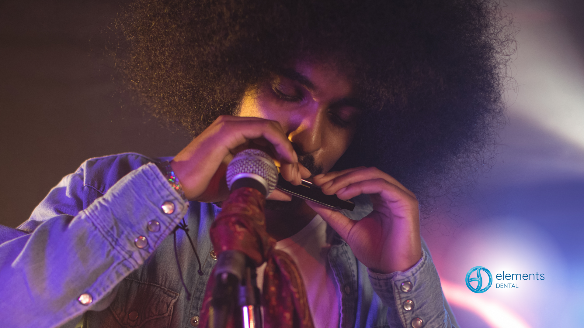 A man with an afro is playing a harmonica in front of a microphone.