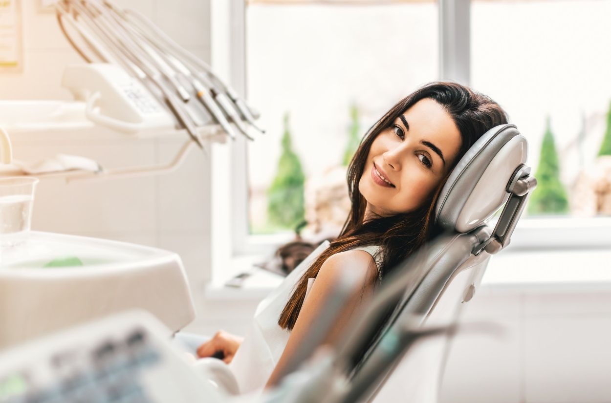 Woman reclining in a dental chair, smiling in a bright clinic while dental tools hang nearby