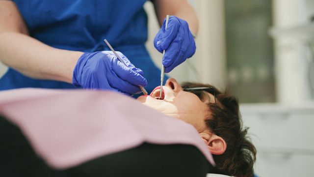 Dentist examining smiling patient with dental tools and gloves