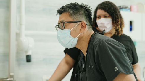 Woman in a blue sweater holding her cheek in a dental office, looking concerned.