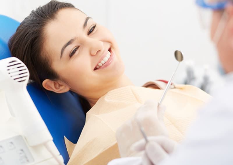 Smiling dental patient reclining in a chair during a checkup, with a dentist tool nearby