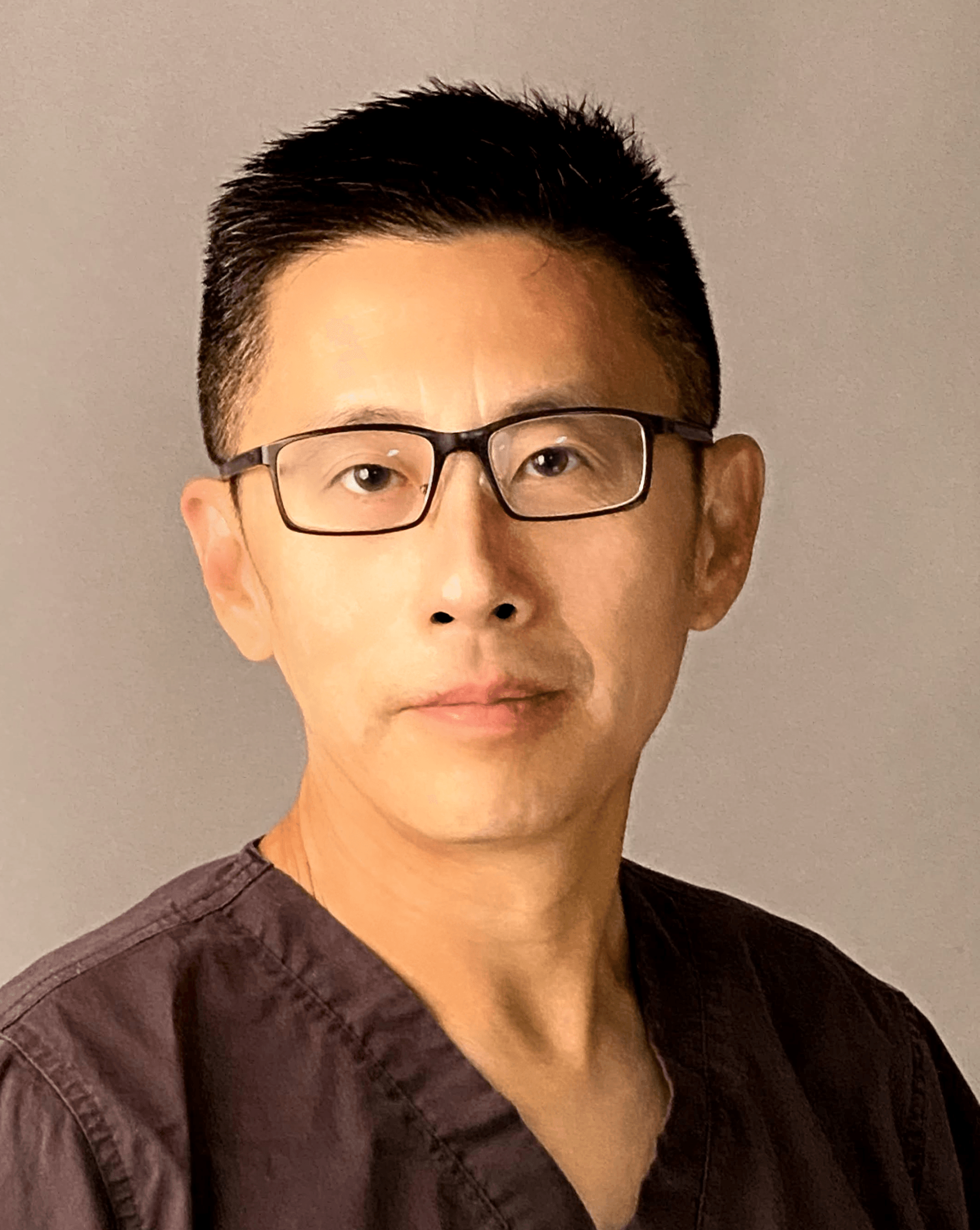 A man wearing glasses and a scrub top is looking at the camera.