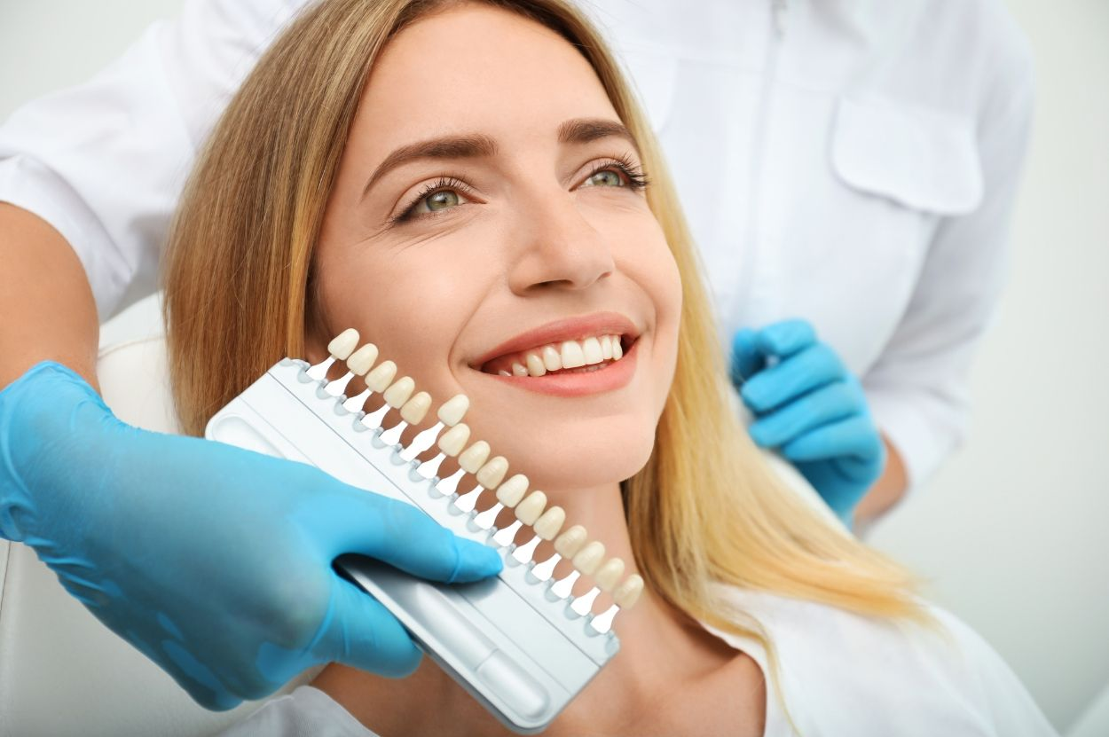 Smiling patient in dental chair as gloved dentist holds tooth shade guide