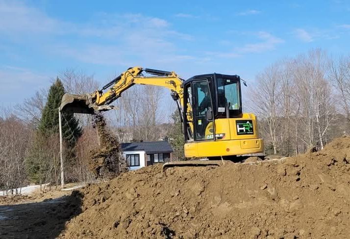 Une pelleteuse jaune creuse une tranchée sur un chantier de construction par une journée ensoleillée.