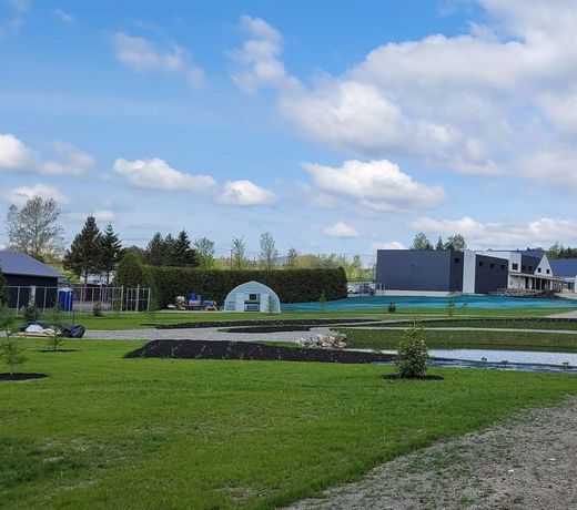 Pelouse verdoyante avec parterres de fleurs, petite serre et maisons modernes sous un ciel bleu.