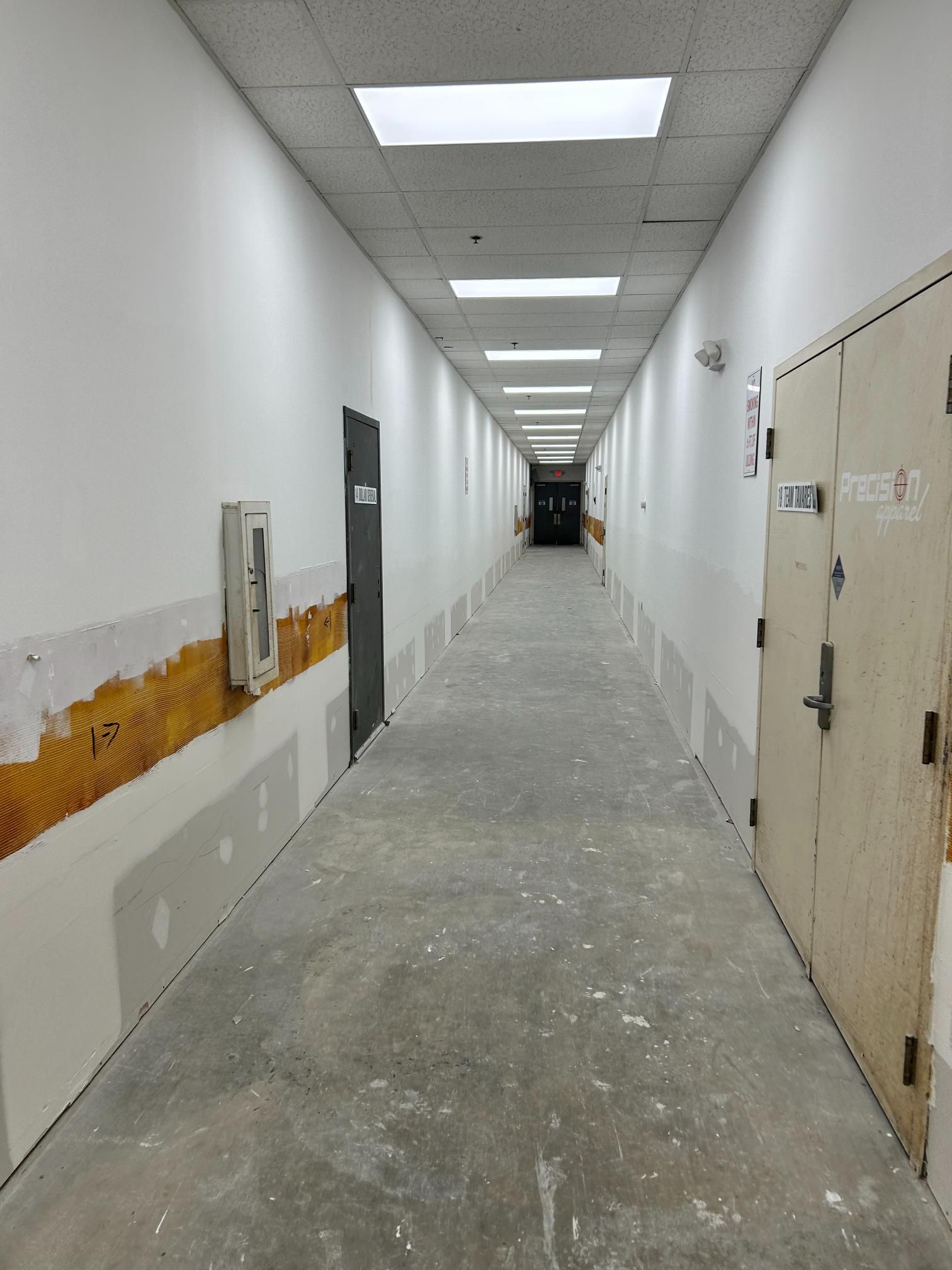 A gray janitorial cleaning cart stocked with spray bottles, cloths, gloves, and a mop in a modern office hallway.