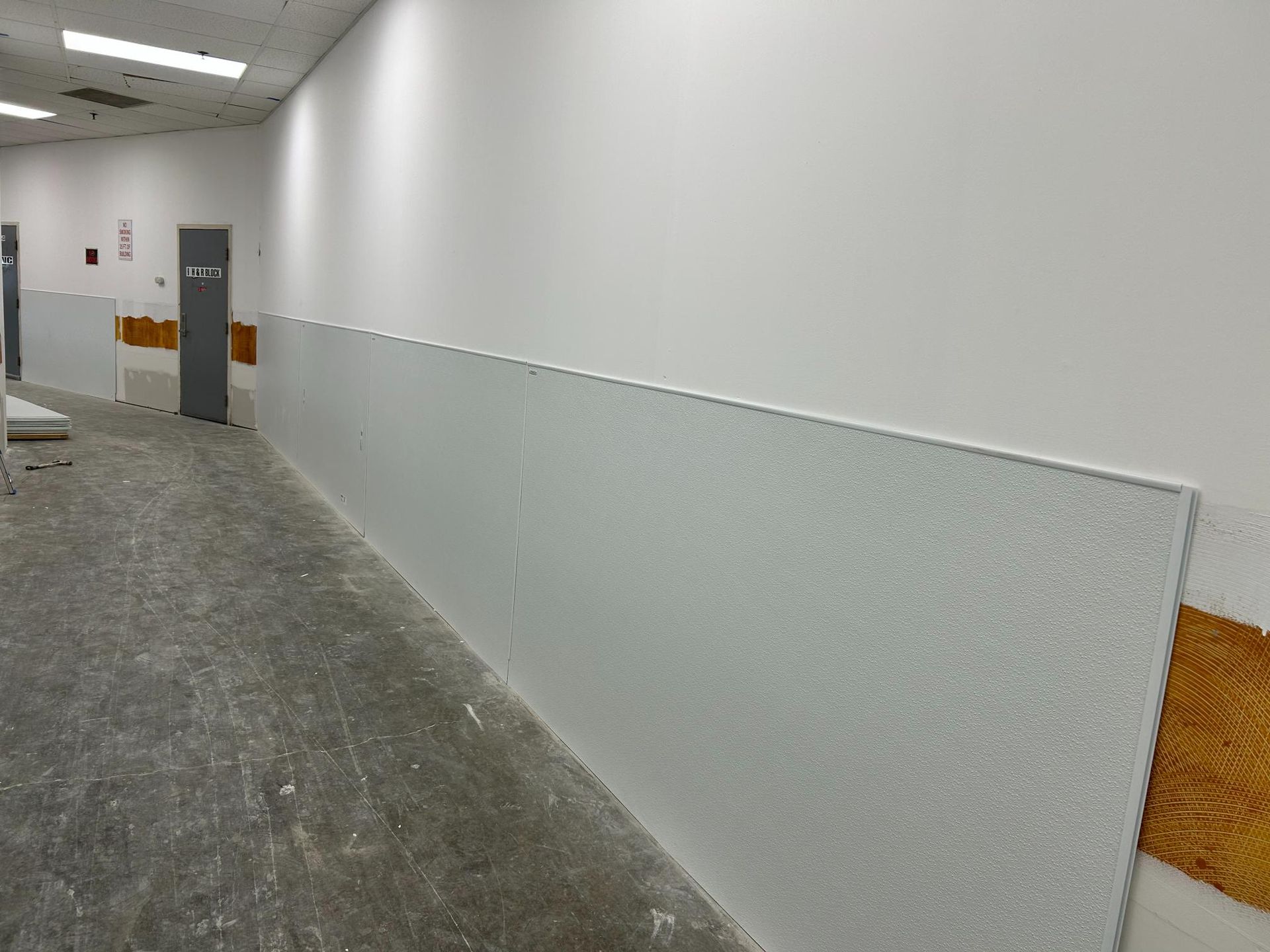 A hallway under construction with unfinished drywall, gray textured wall panels, and exposed wood paneling on the walls.