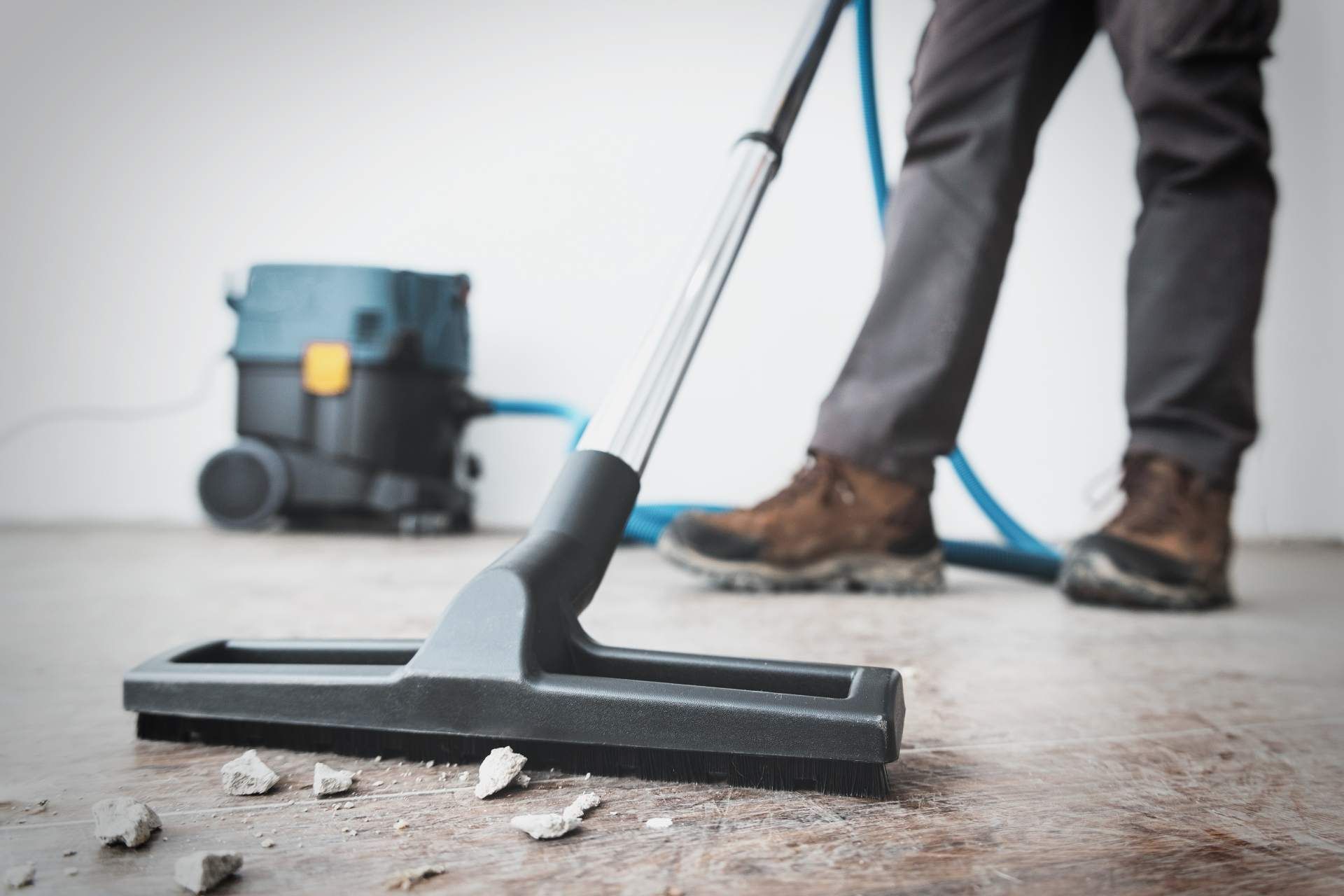 A person using a professional vacuum to clean dust and debris off a concrete floor.