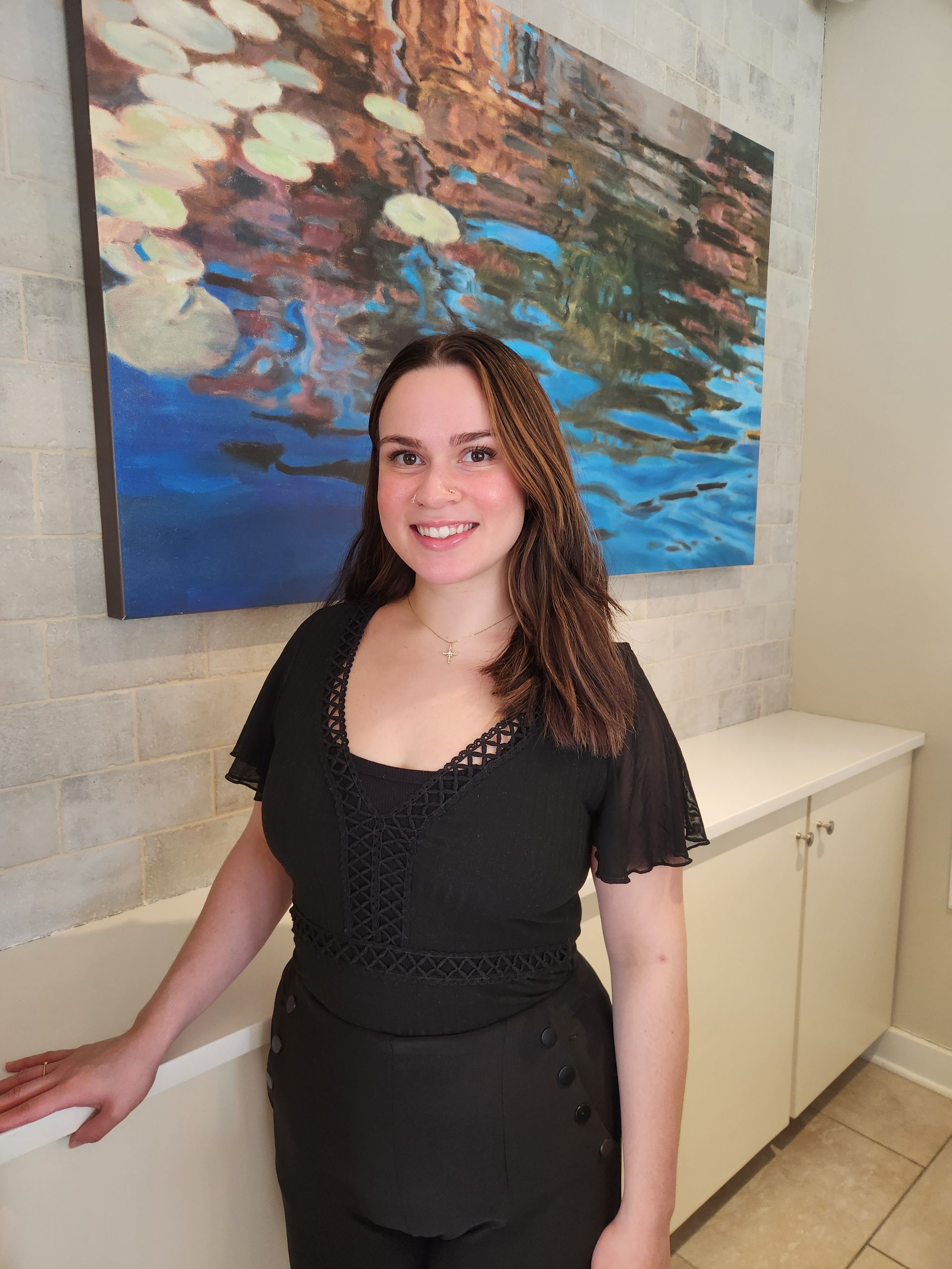 A woman in a black shirt is standing in front of a painting.