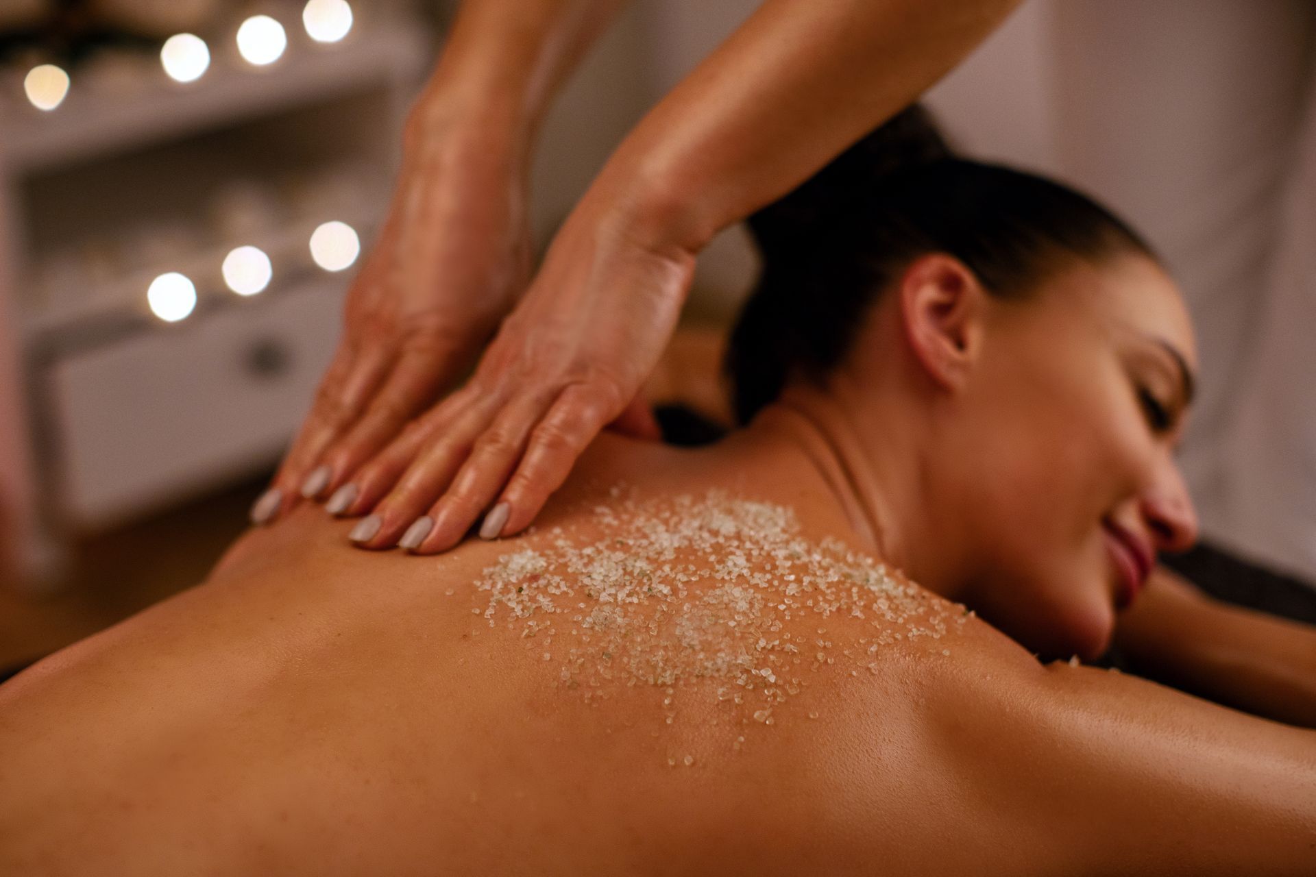 Person receiving a shoulder massage with salt scrub in a dim spa setting