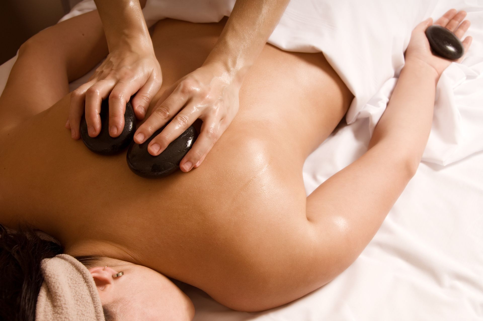 Massage therapist using hot stones on a client's back during a spa treatment