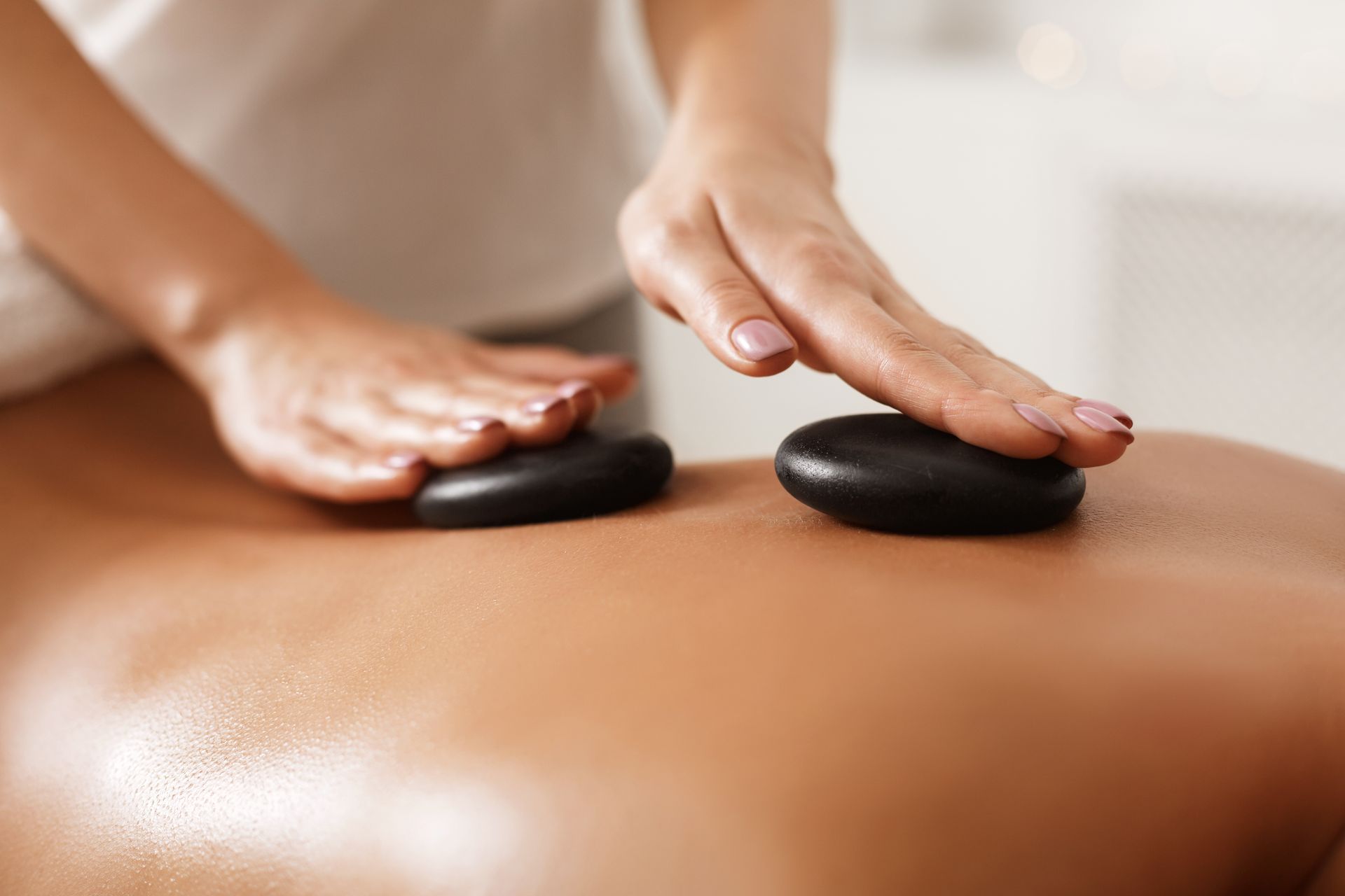 Two hands placing hot stones on a person’s bare back during a massage