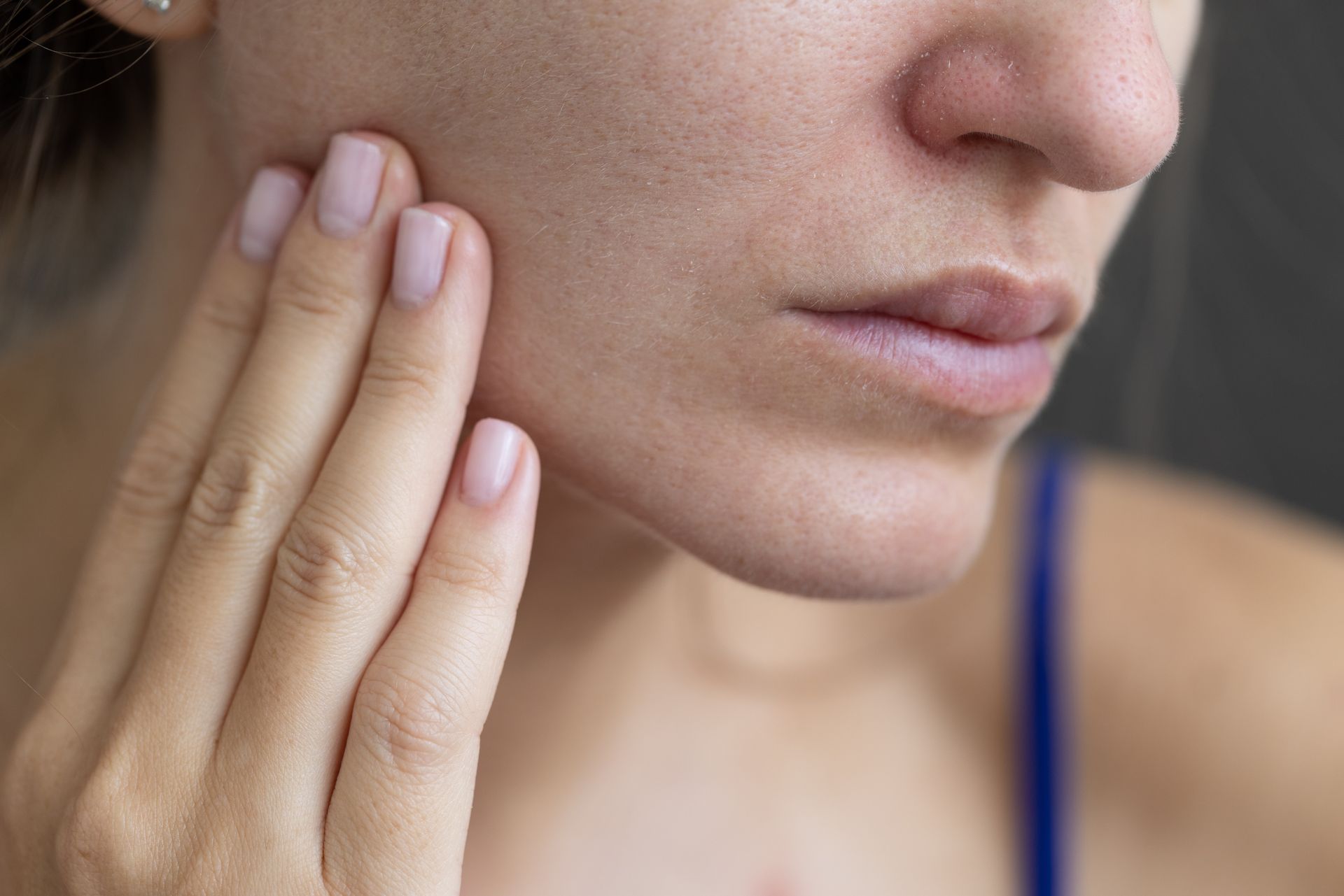 Close-up of a person touching their cheek and jaw with a concerned expression