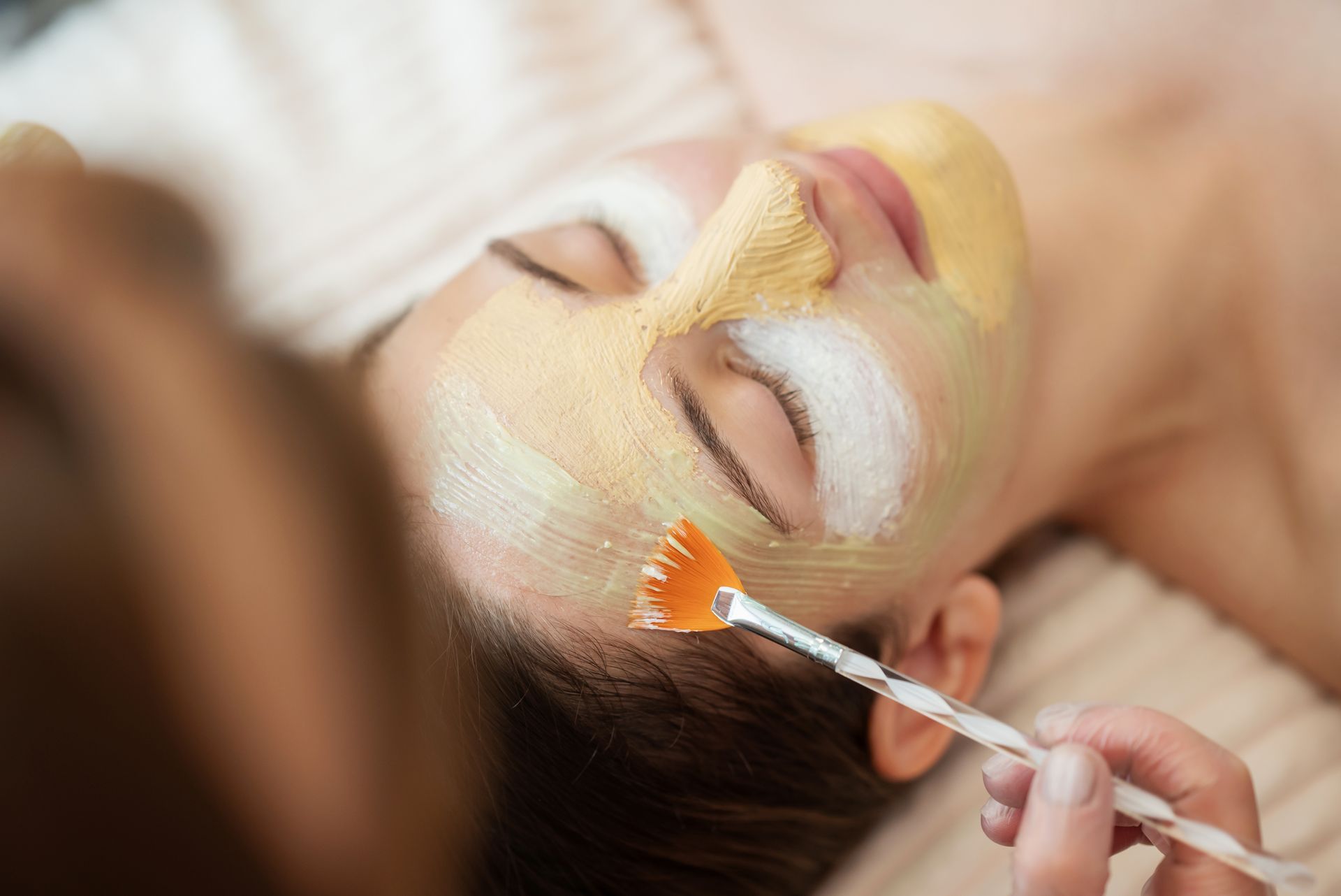 Person applying a facial mask with a brush while lying down, eyes closed