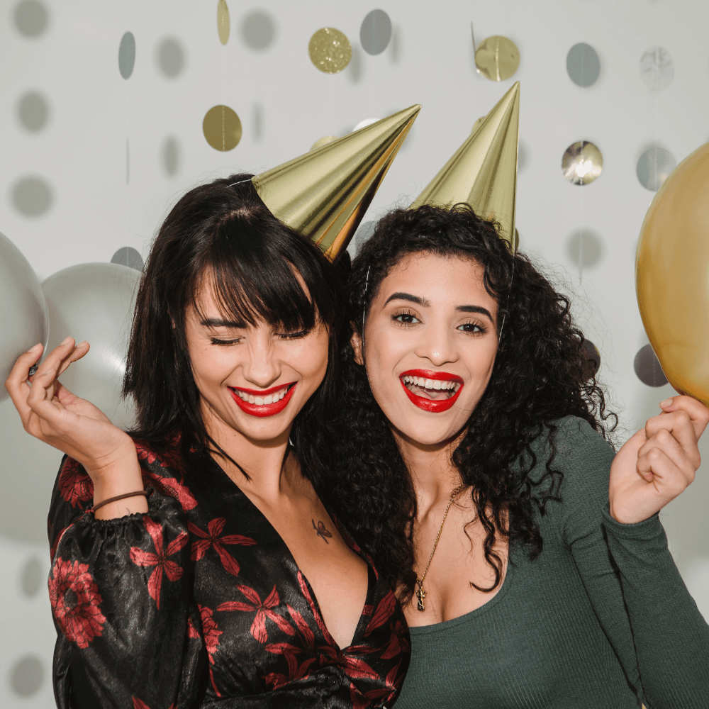 Two women wearing party hats and holding balloons