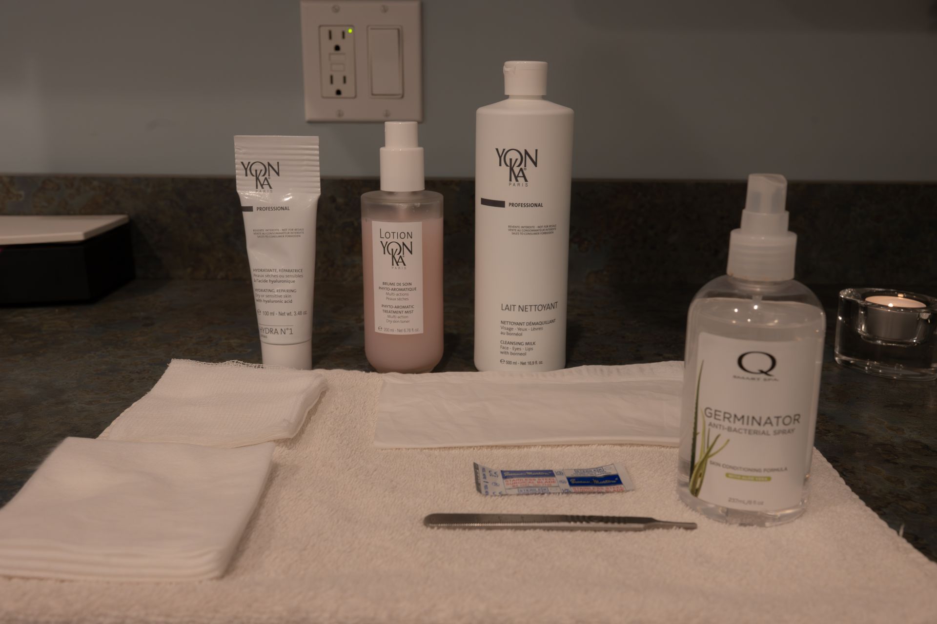 Bathroom counter with toiletry bottles, folded towels, and a toothbrush on a white mat.