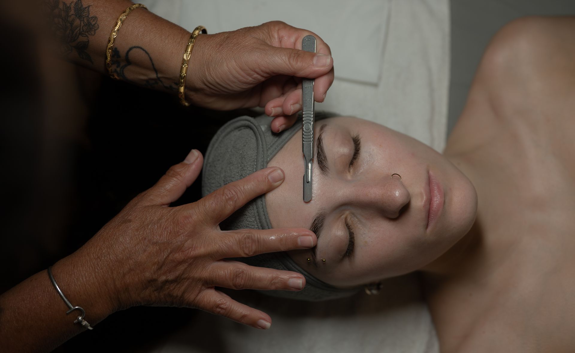 Hands hold a woman's face while a wand is drawn across her closed eyes in a spa treatment