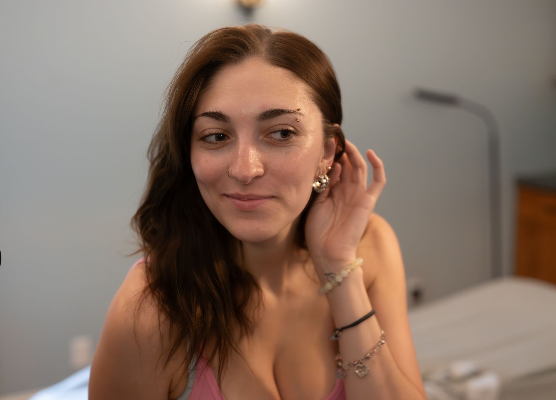 Woman smiling and touching her ear while sitting in a softly lit bedroom
