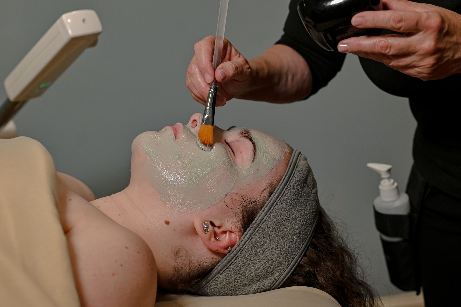 Facial treatment with a therapist using a brush to apply product on a client’s face