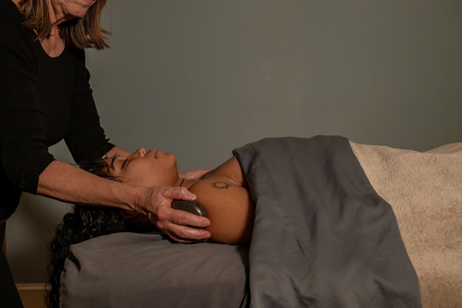 Woman receiving a head massage while lying on a treatment table, covered with a gray blanket.