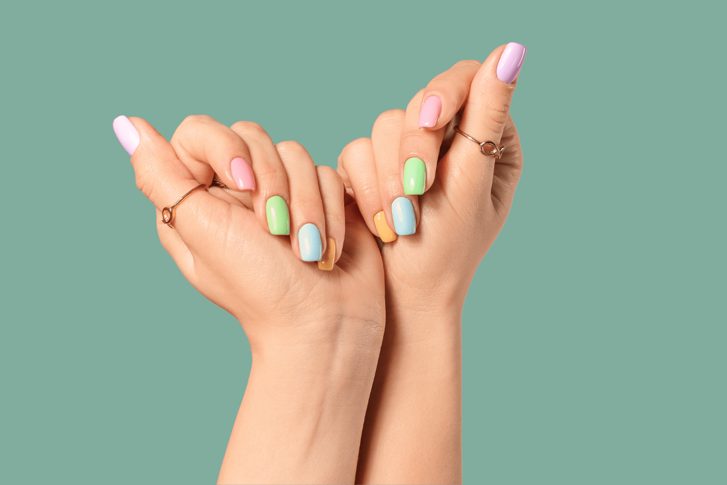 A woman 's hands with colorful nails and rings on a green background.