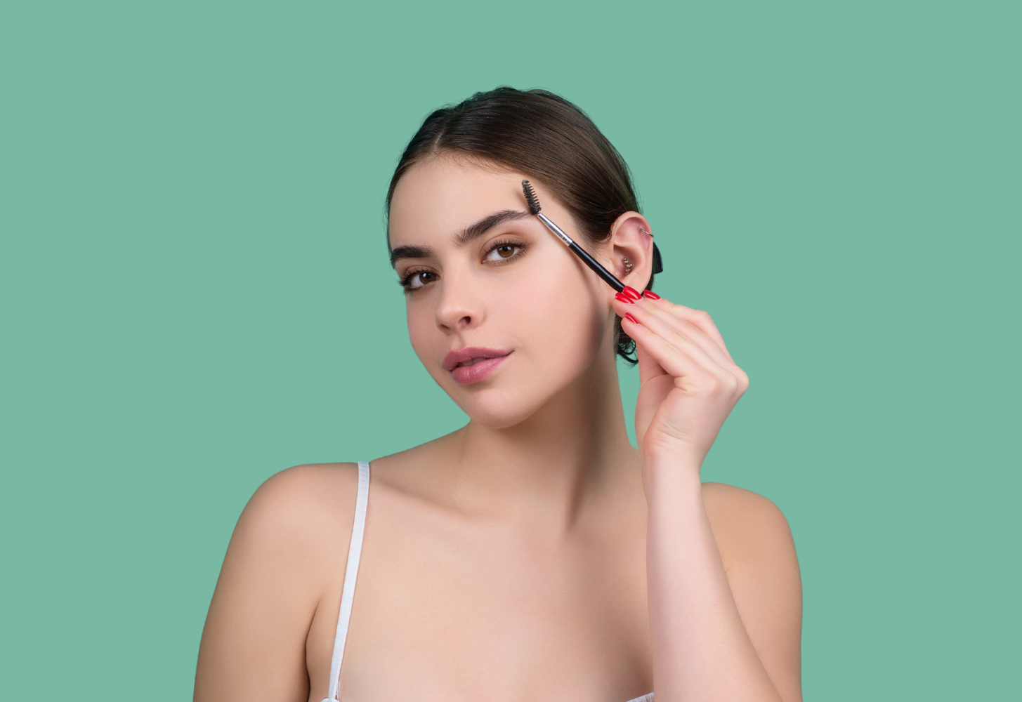 Woman brushing eyebrow with a makeup brush, green background.