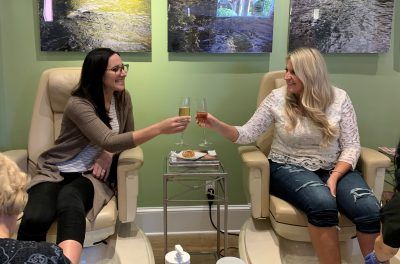 Two women are sitting in chairs toasting with champagne.
