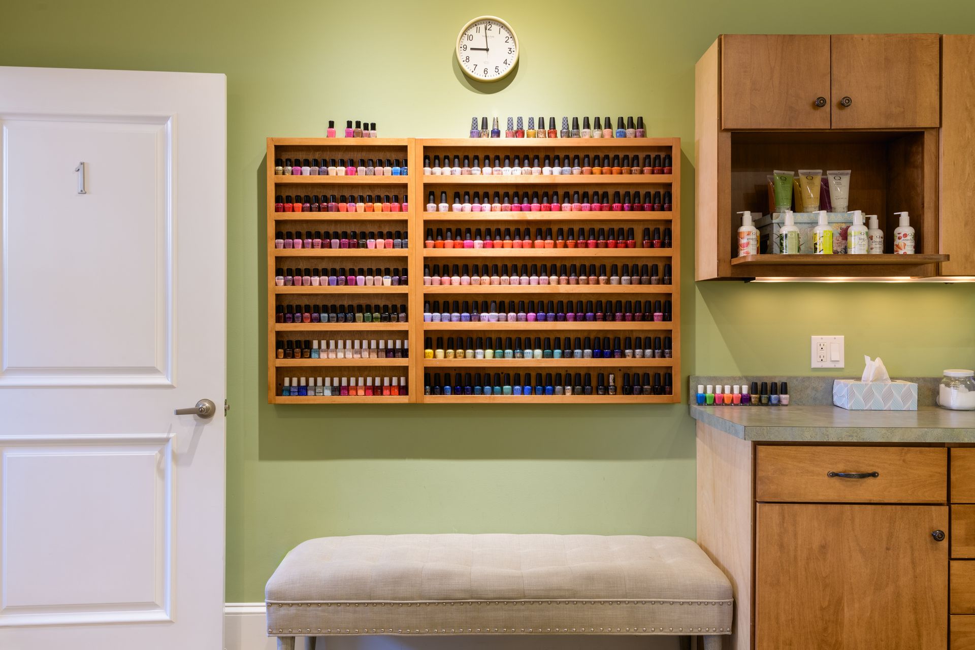 There is a clock on the wall above the shelves of nail polish.