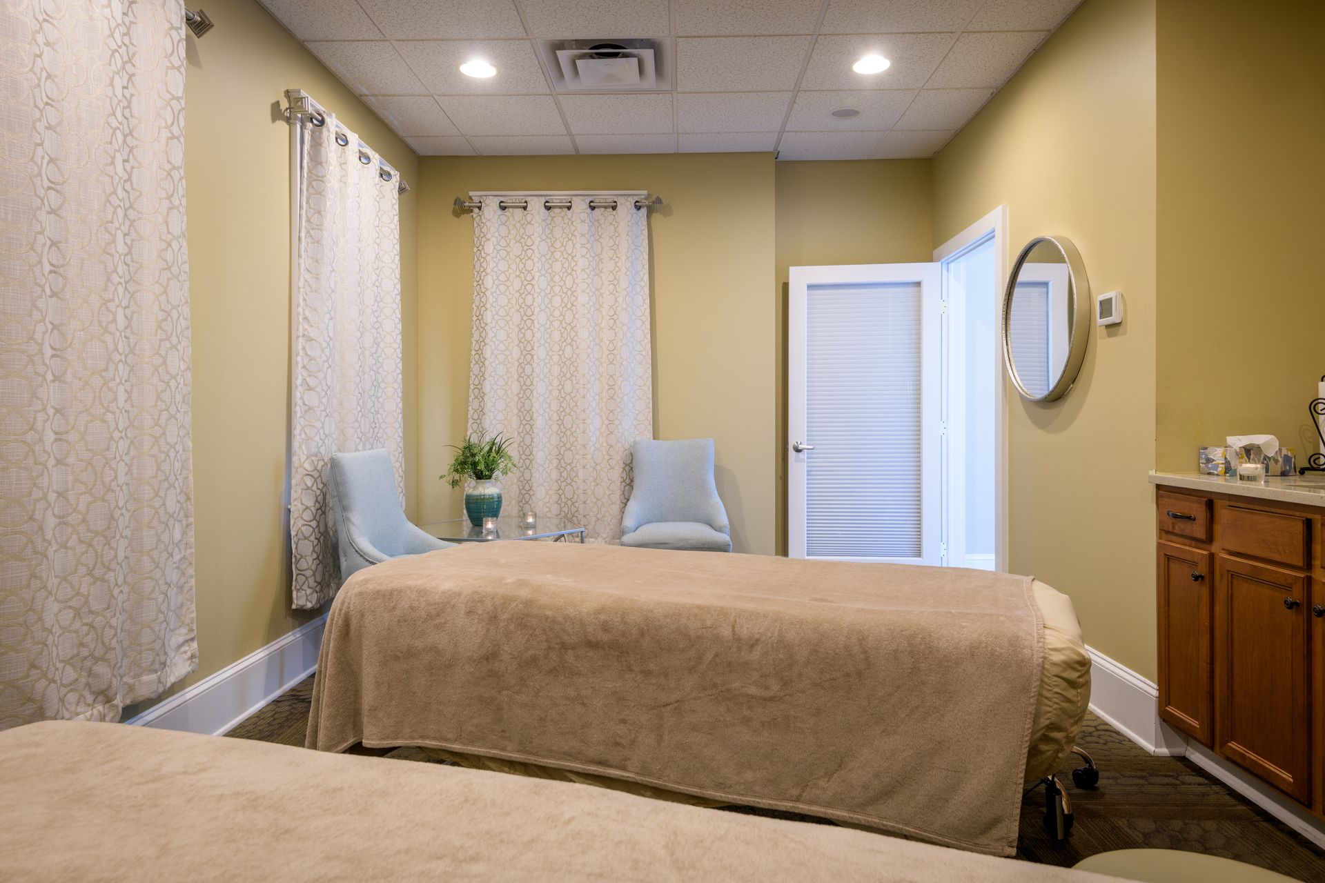 A massage room with two beds , chairs and a mirror.