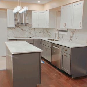 Modern kitchen with white cabinets, marble backsplash, stainless appliances, and a central island with a white countertop