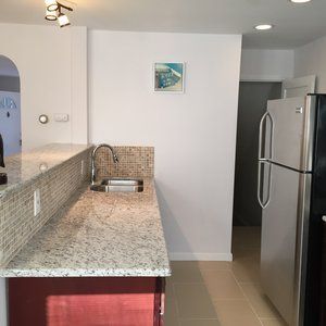 Kitchen with granite breakfast bar, mosaic backsplash, and stainless steel refrigerator in a narrow, bright room