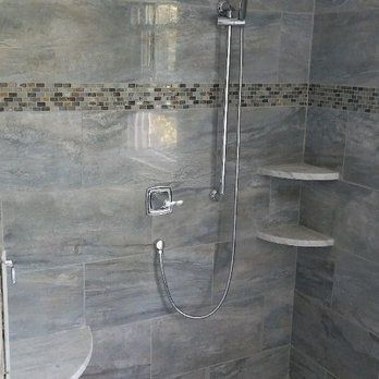 Modern tiled shower with chrome showerhead, handheld sprayer, and corner shelves