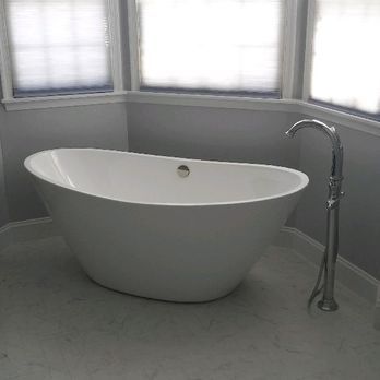 White freestanding bathtub beside chrome floor faucet in a bright tiled bathroom