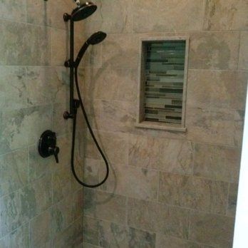 Walk-in shower with tiled walls, black showerhead, and a small recessed shelf with mosaic accent tiles