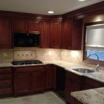 Dark wood kitchen with granite counters, gas stove, beige tile backsplash, and sink by a window.